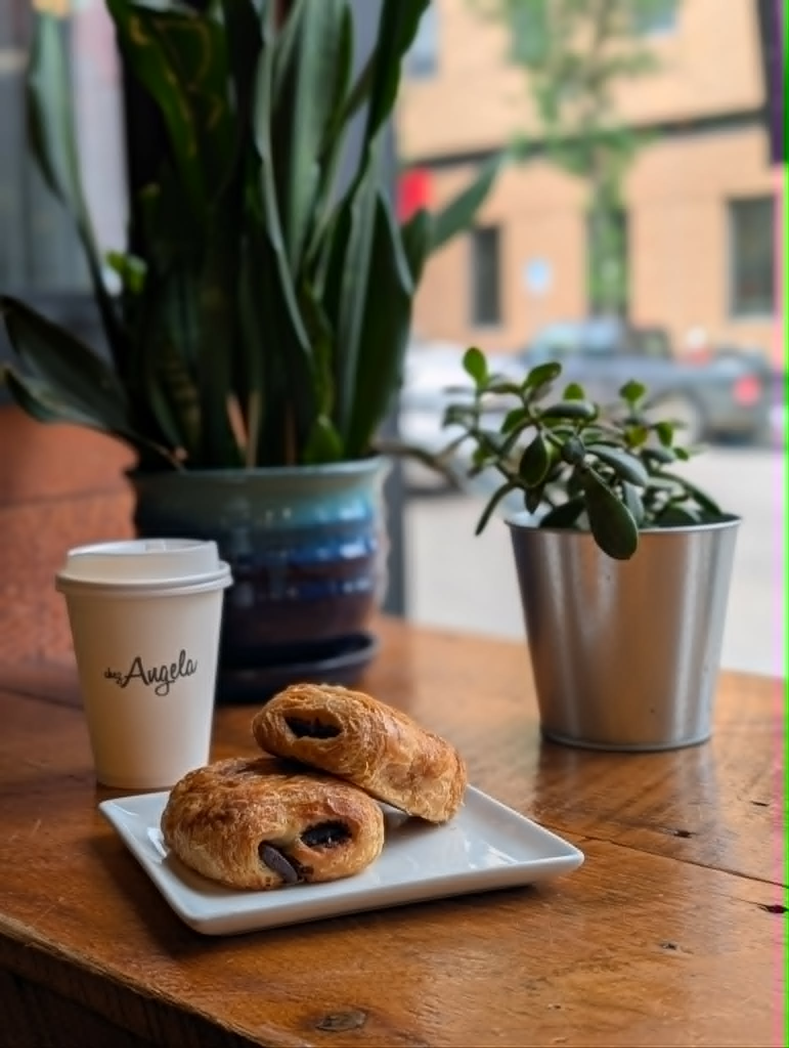 Chez Angela coffee cup, pastries, and plants on a warm cafe table