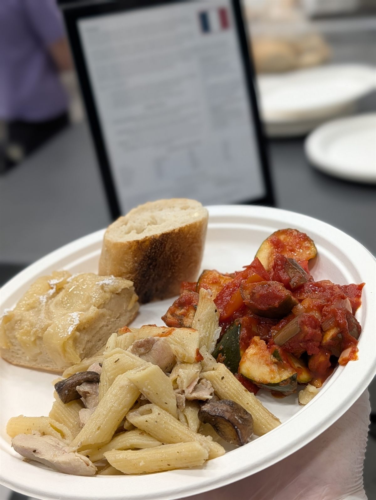 A school lunch style sample plate with pasta, bread, and roasted vegetables